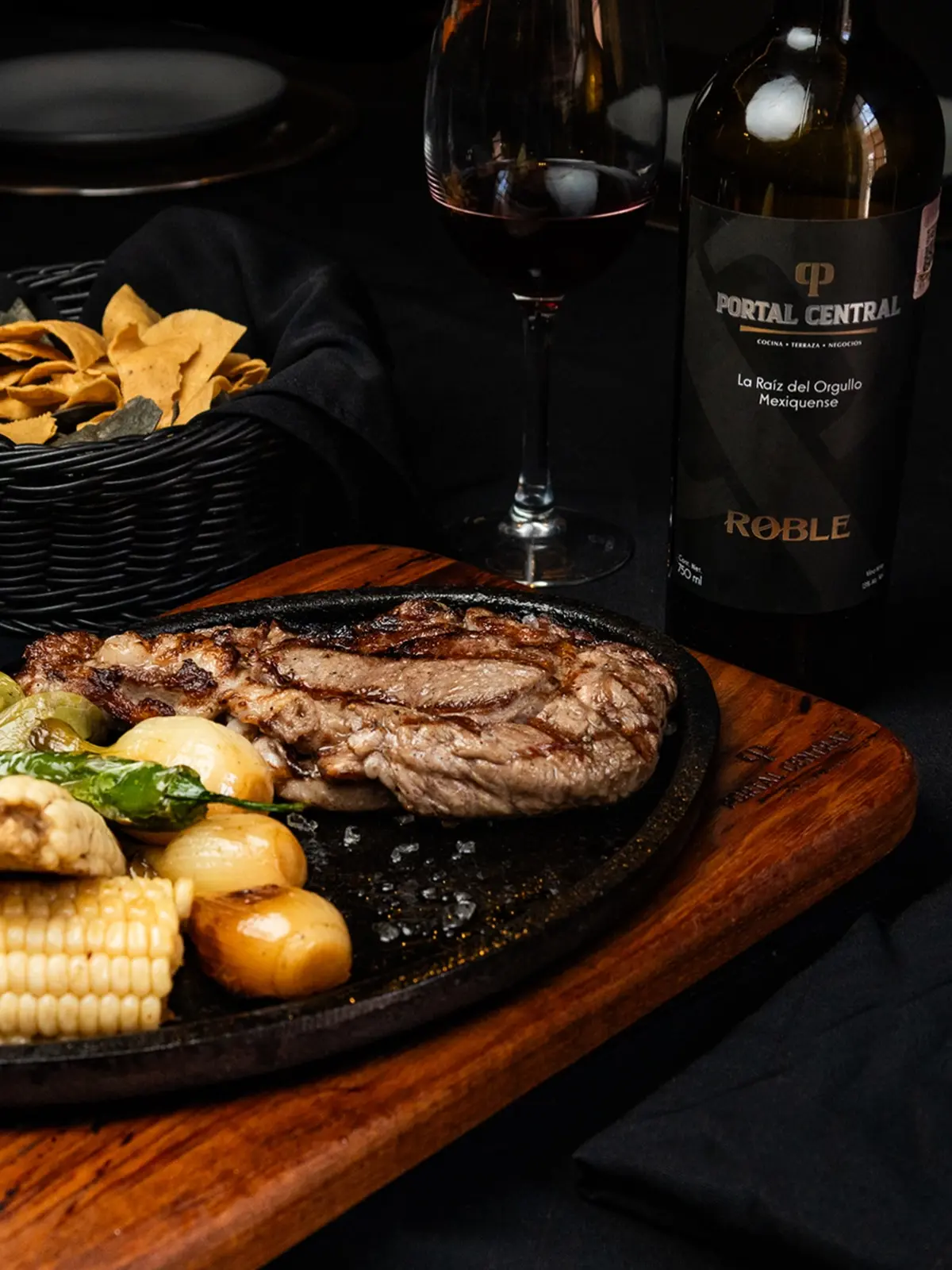 Corte a la parrilla con elote y papas, y botella de vino de la casa