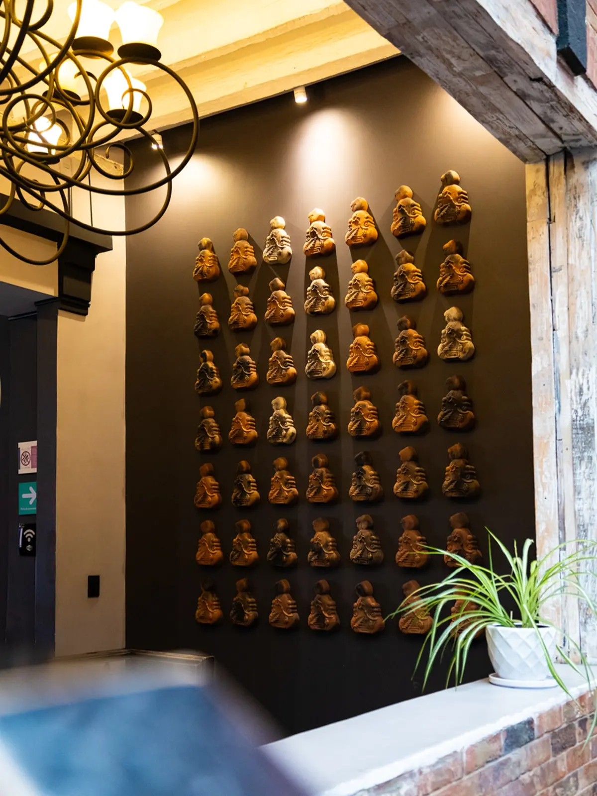 Muro con figuras de barro iluminadas bajo un candil de hierro