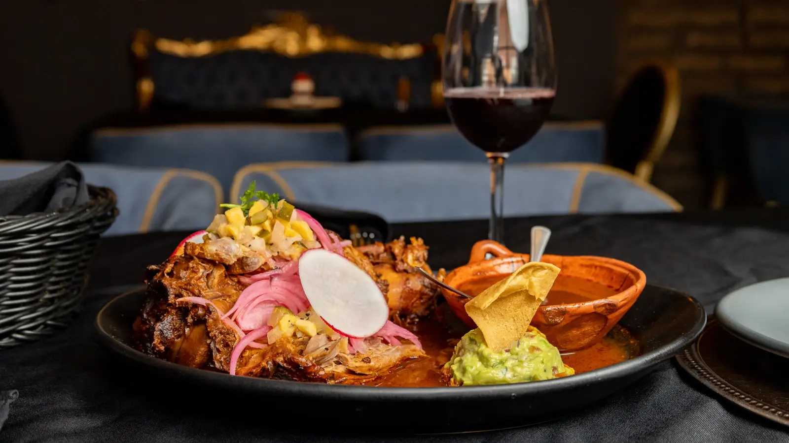 Platillo y copa de vino tinto frente a una sala con respaldo dorado